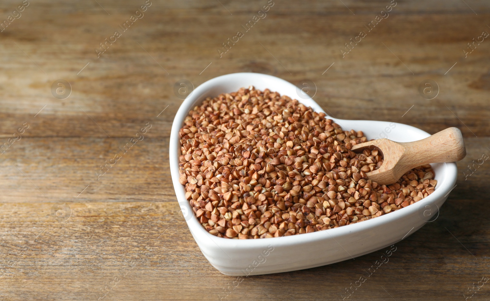 Photo of Uncooked organic buckwheat grains on wooden table. Space for text