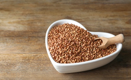 Photo of Uncooked organic buckwheat grains on wooden table. Space for text