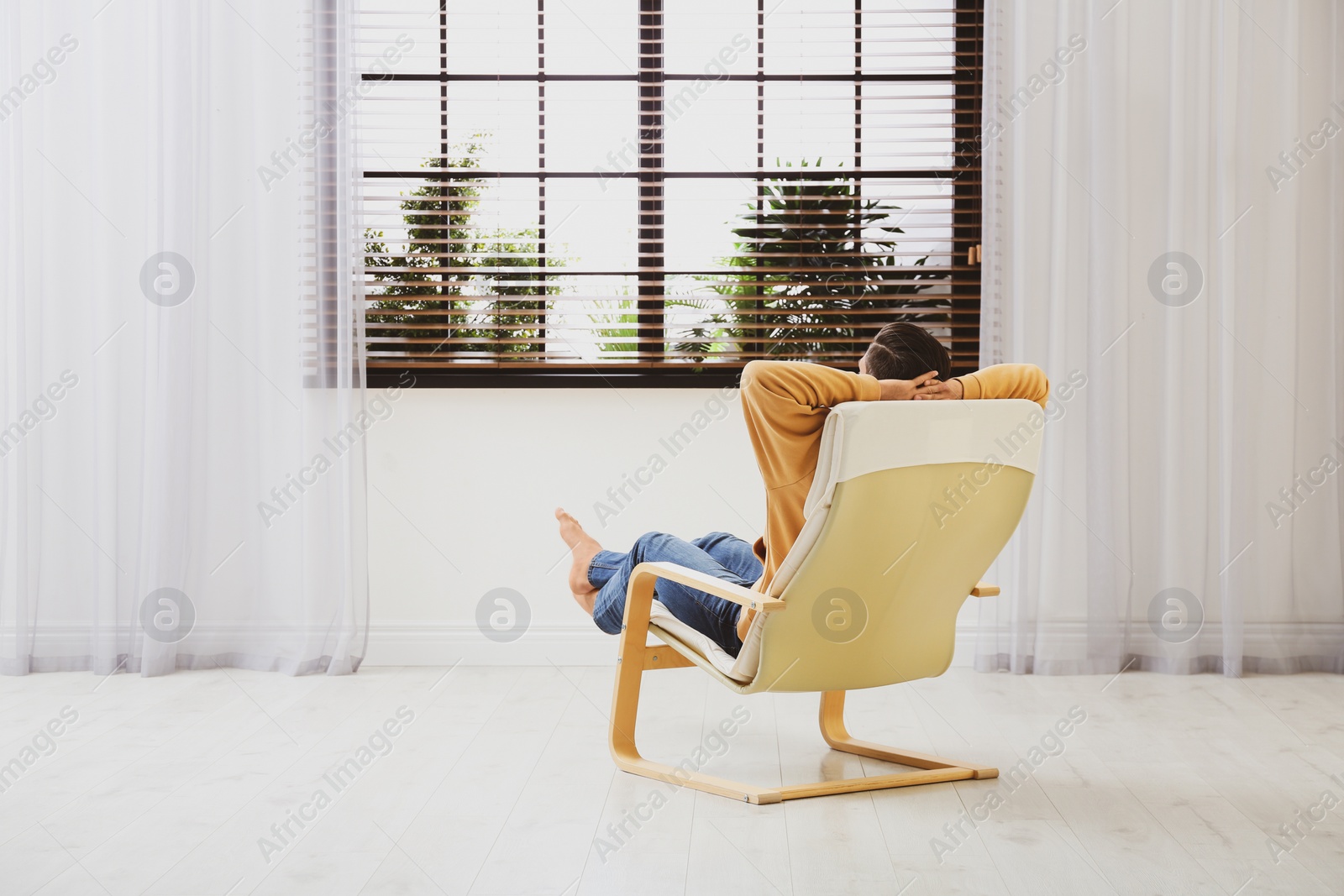 Photo of Man relaxing in armchair near window at home, back view