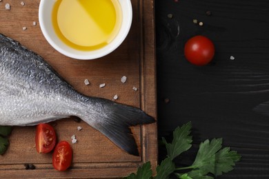 Photo of Raw dorado fish, spices, tomatoes and oil on black wooden table, flat lay