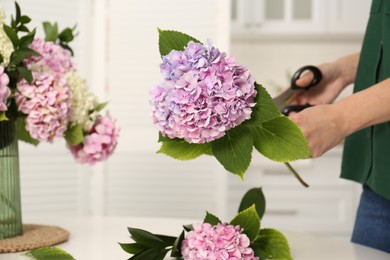 Woman pruning stem of hydrangea flower indoors, closeup. Interior design element