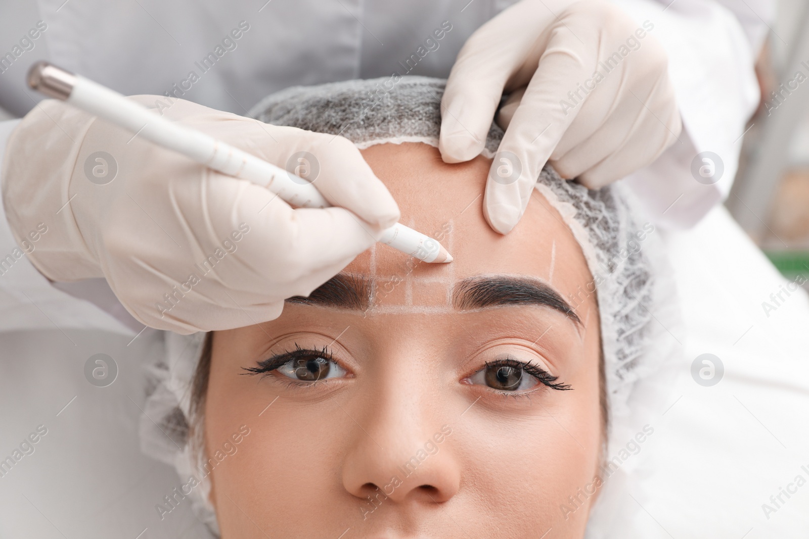 Photo of Young woman getting prepared for procedure of permanent eyebrow makeup in tattoo salon, closeup