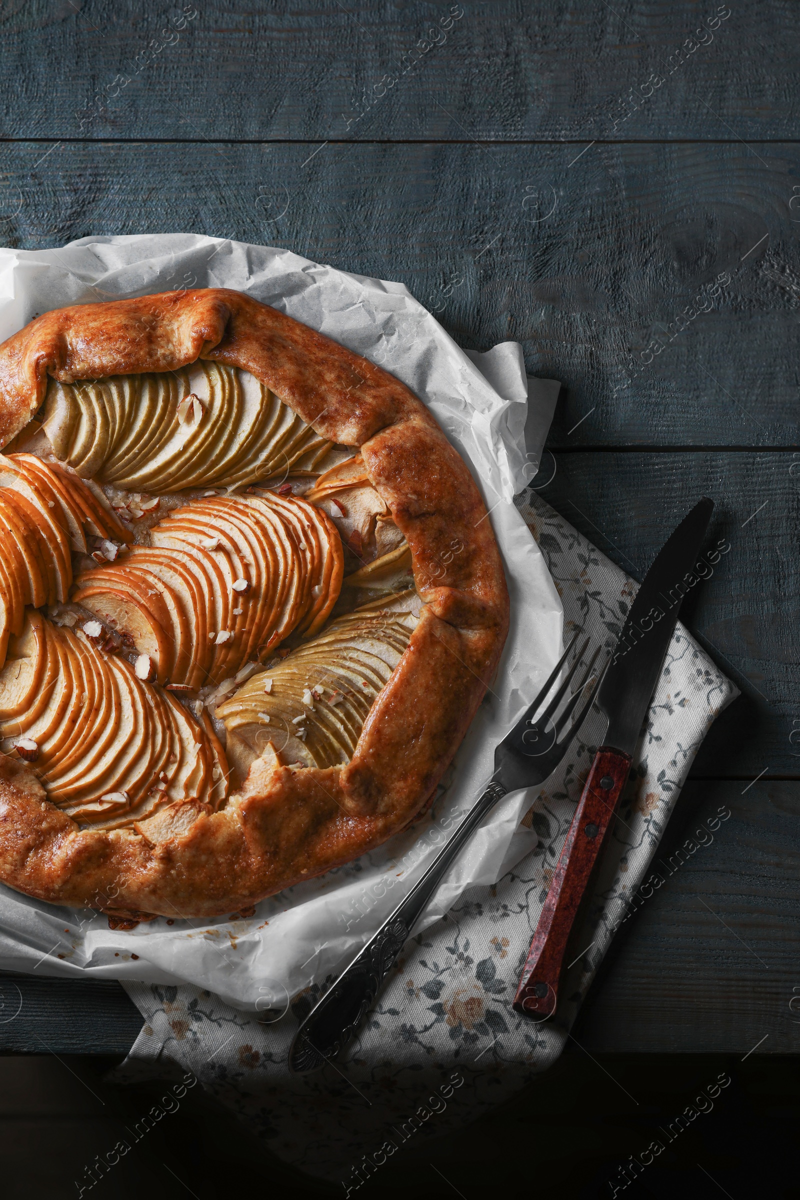 Photo of Delicious apple galette with walnuts, knife and fork on wooden table, flat lay