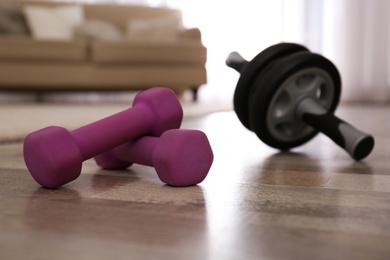 Photo of Pink dumbbells and abs roller on floor in room. Home fitness