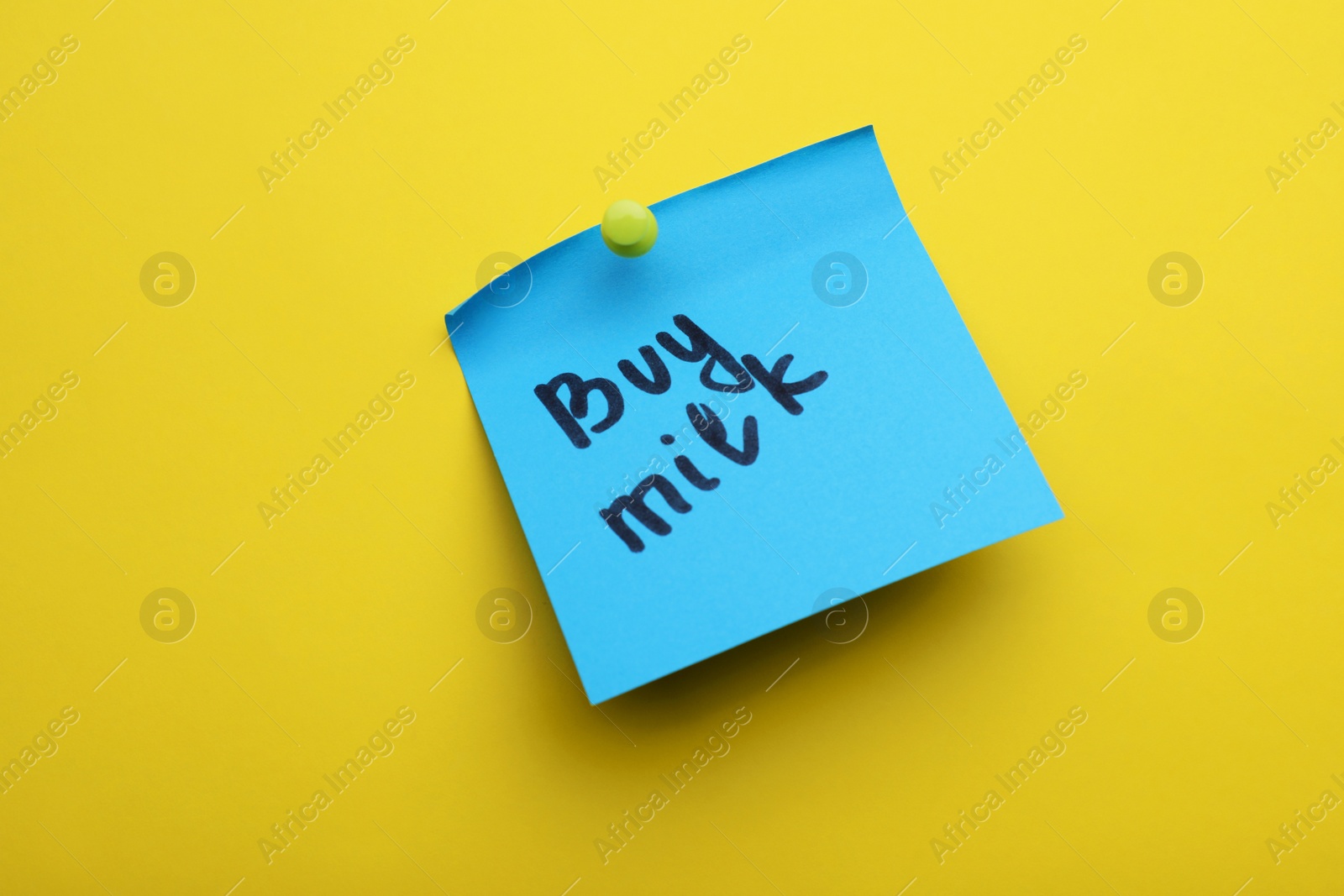 Photo of Paper note with words Buy milk pinned on yellow background