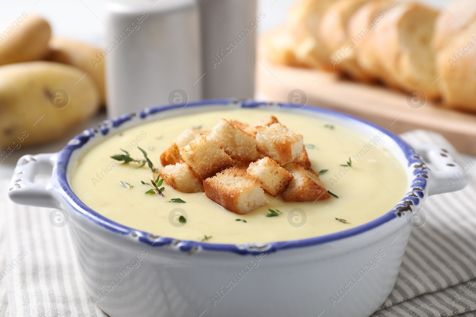 Photo of Tasty potato soup with croutons and rosemary in ceramic pot on white table, closeup