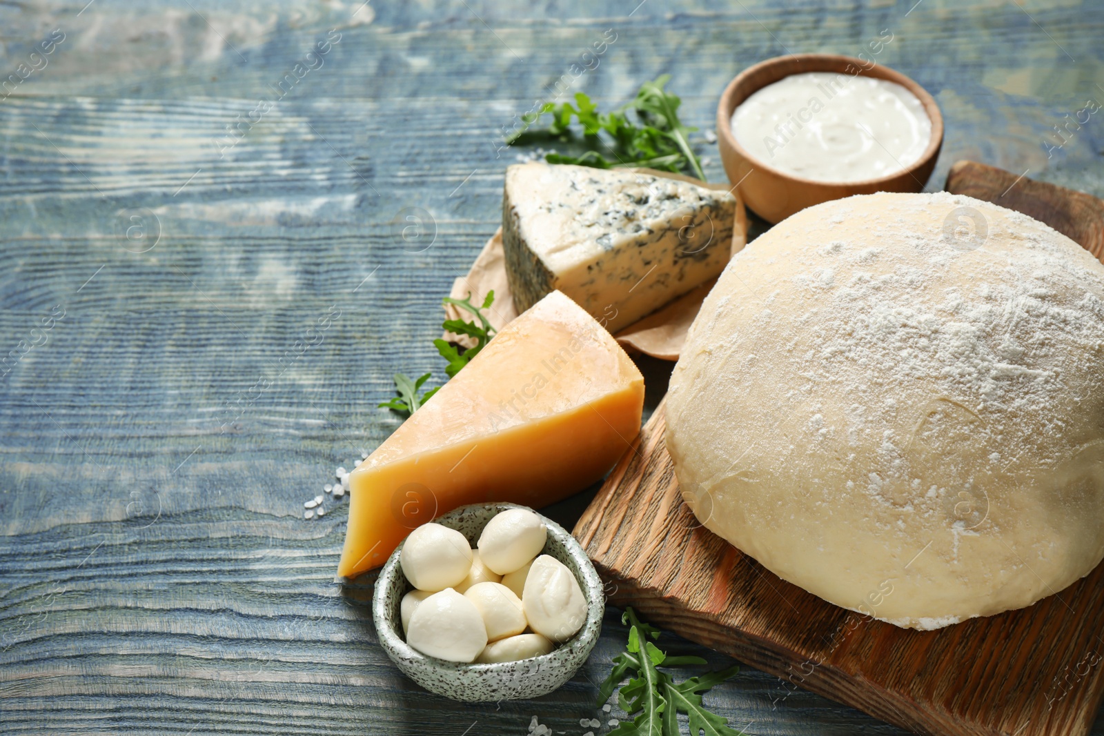 Photo of Fresh dough and pizza ingredients on blue wooden table. Space for text