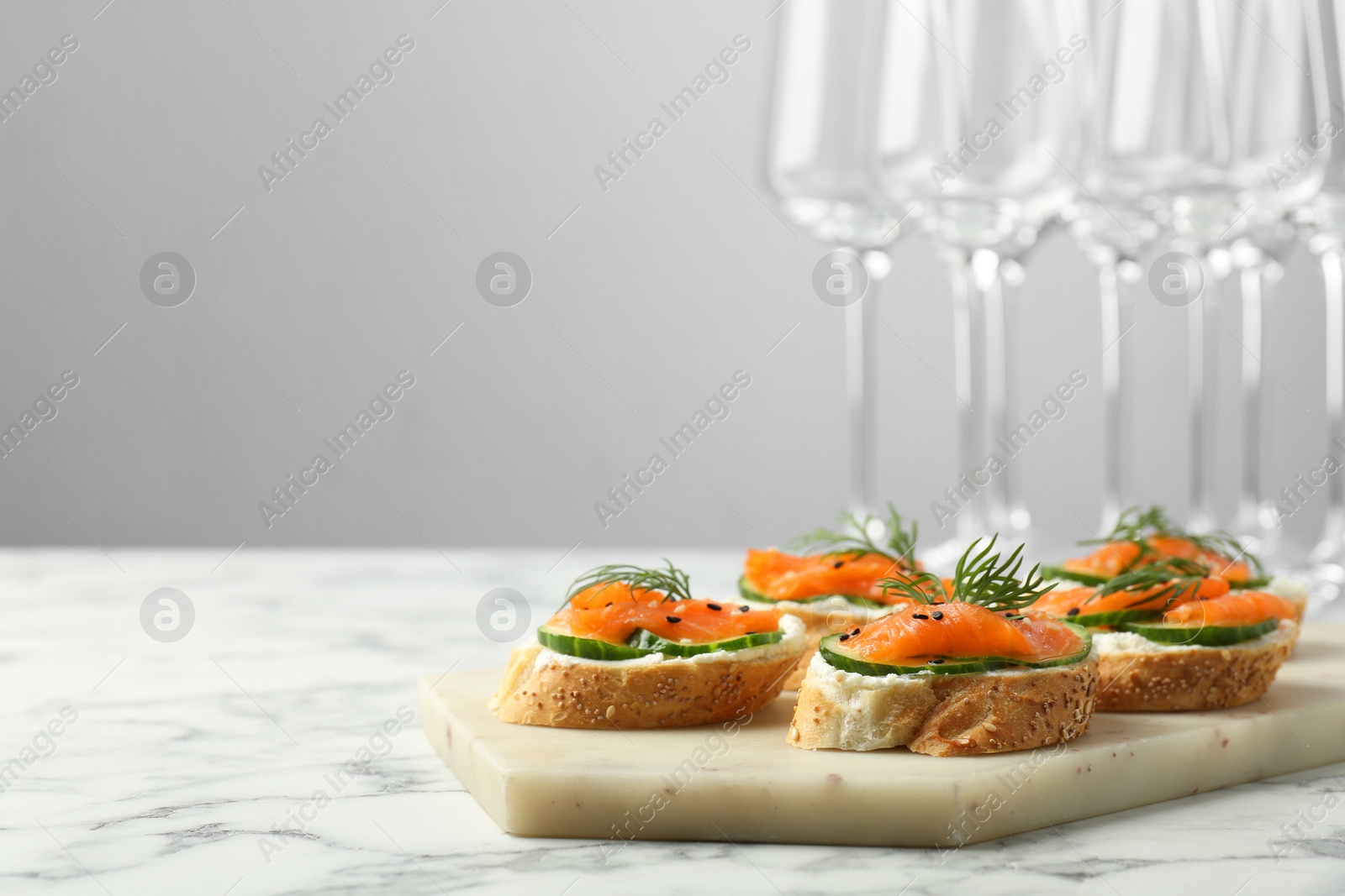 Photo of Tasty canapes with salmon, cucumber and cream cheese on white marble table. Space for text