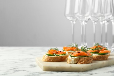 Photo of Tasty canapes with salmon, cucumber and cream cheese on white marble table. Space for text