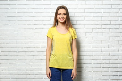 Young woman wearing blank t-shirt near white brick wall. Mockup for design