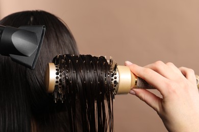 Photo of Hairdresser blow drying client's hair on light brown background, closeup