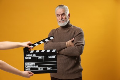 Photo of Senior actor performing while second assistant camera holding clapperboard on yellow background. Film industry