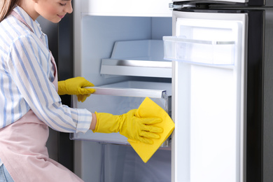 Photo of Woman in rubber gloves cleaning refrigerator, closeup