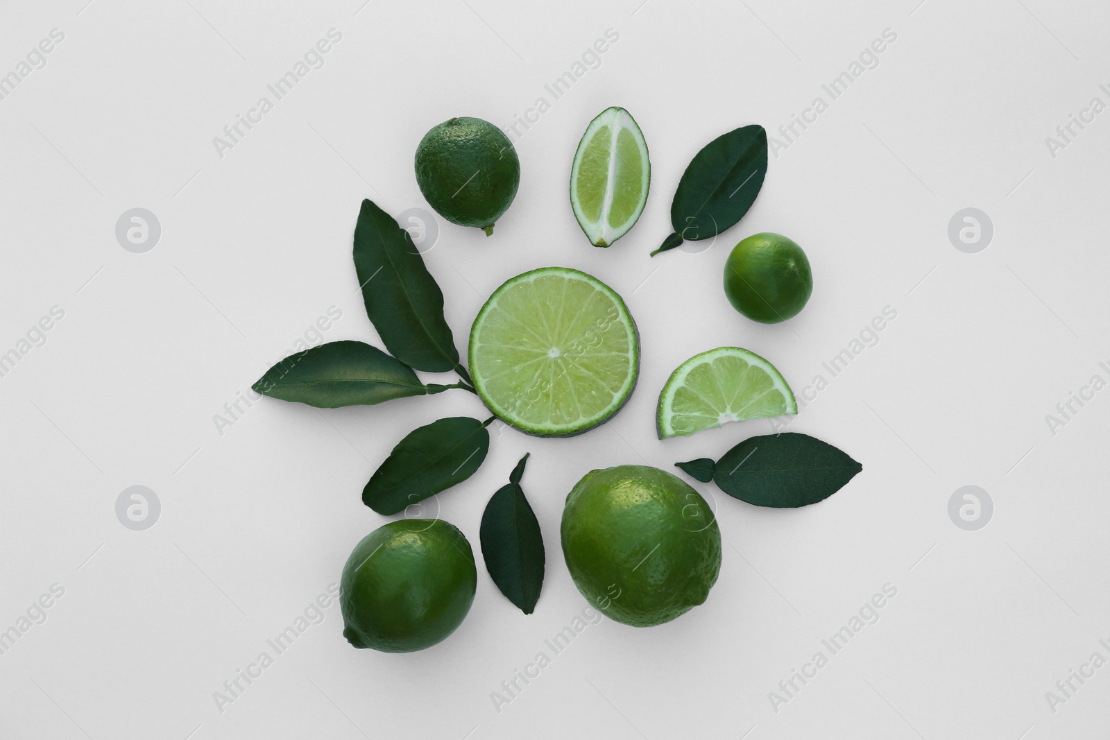 Photo of Whole and cut fresh limes with leaves on white background, flat lay