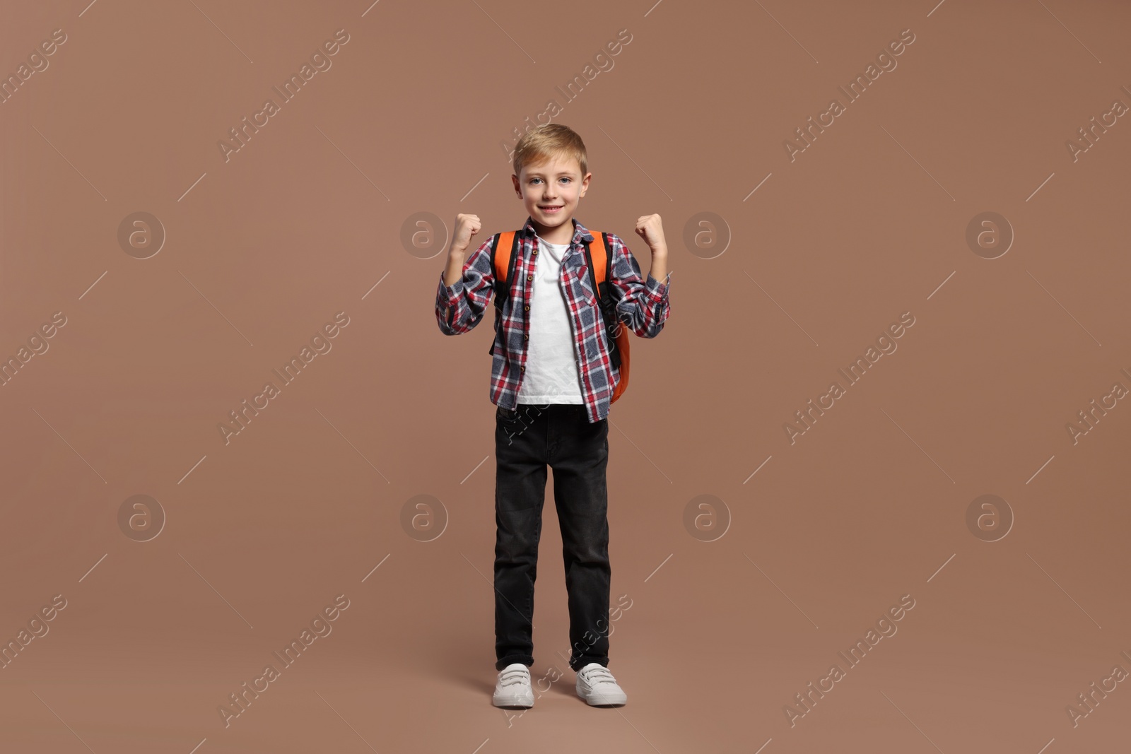 Photo of Happy schoolboy with backpack on brown background