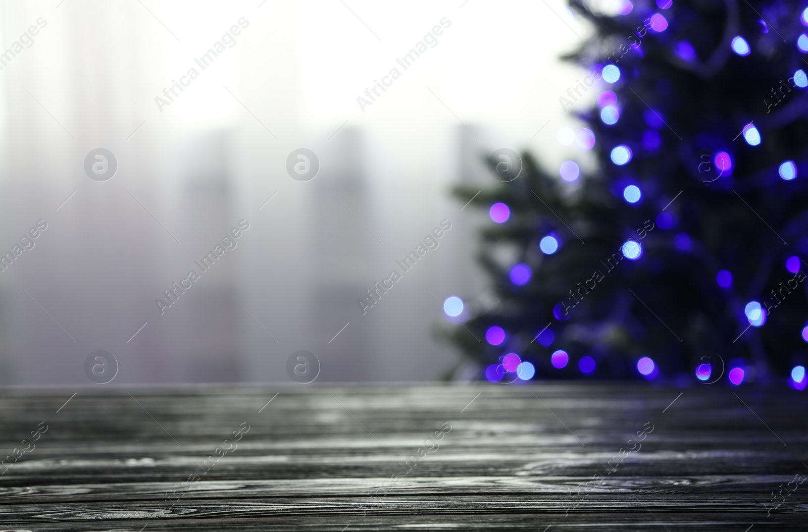 Photo of Empty table and blurred fir tree with violet Christmas lights on background, bokeh effect. Space for design