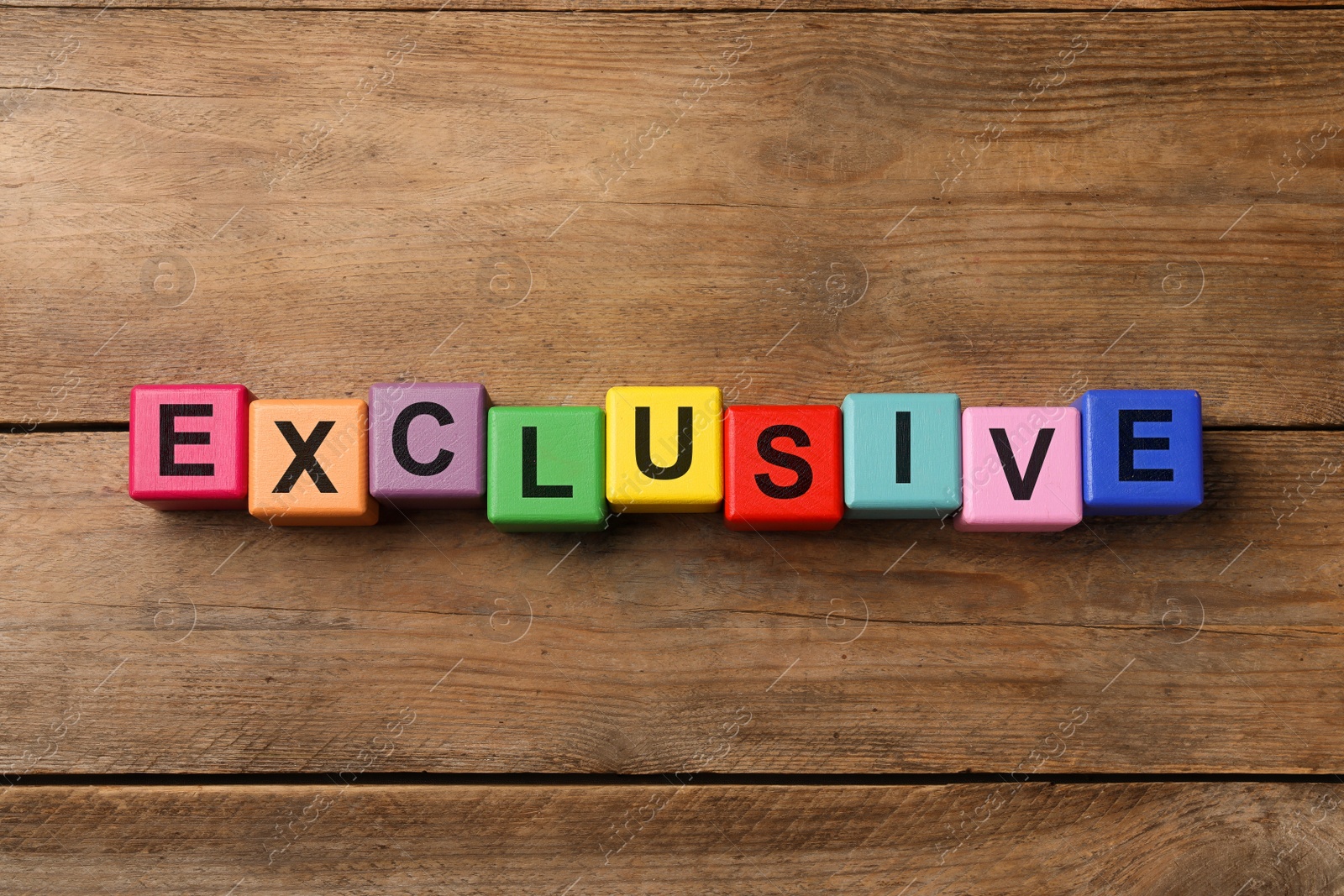 Photo of Colorful cubes with word Exclusive on wooden table, flat lay