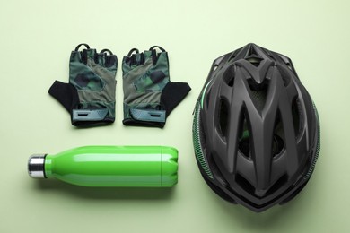 Photo of Bicycle helmet, fingerless gloves and bottle on light background, flat lay