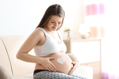 Pregnant woman with heart painted on her belly against blurred background