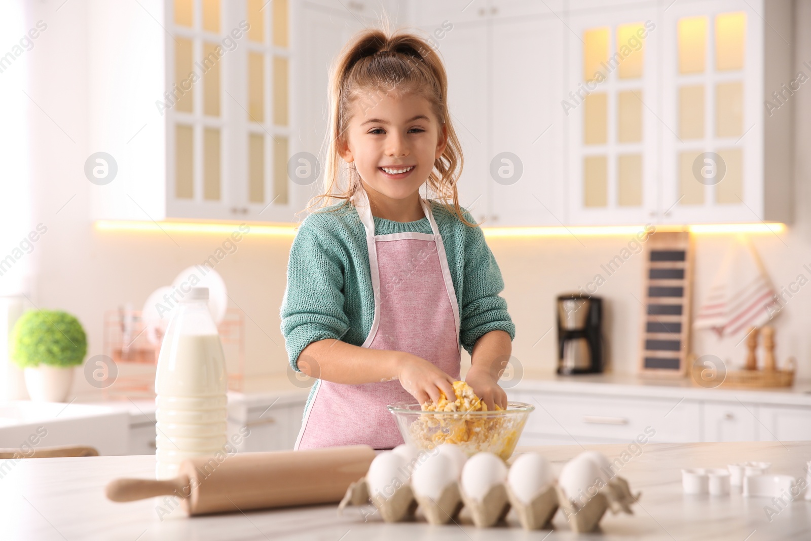 Photo of Little girl making dough at table in kitchen