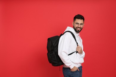 Young man with stylish backpack on red background. Space for text
