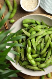 Photo of Green edamame beans in pods served with sesame seeds on wooden table, flat lay