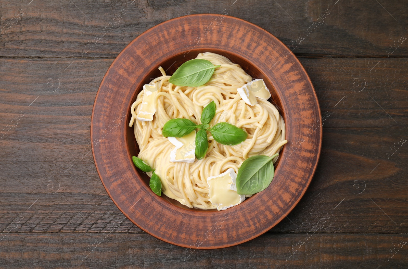 Photo of Delicious pasta with brie cheese and basil leaves on wooden table, top view