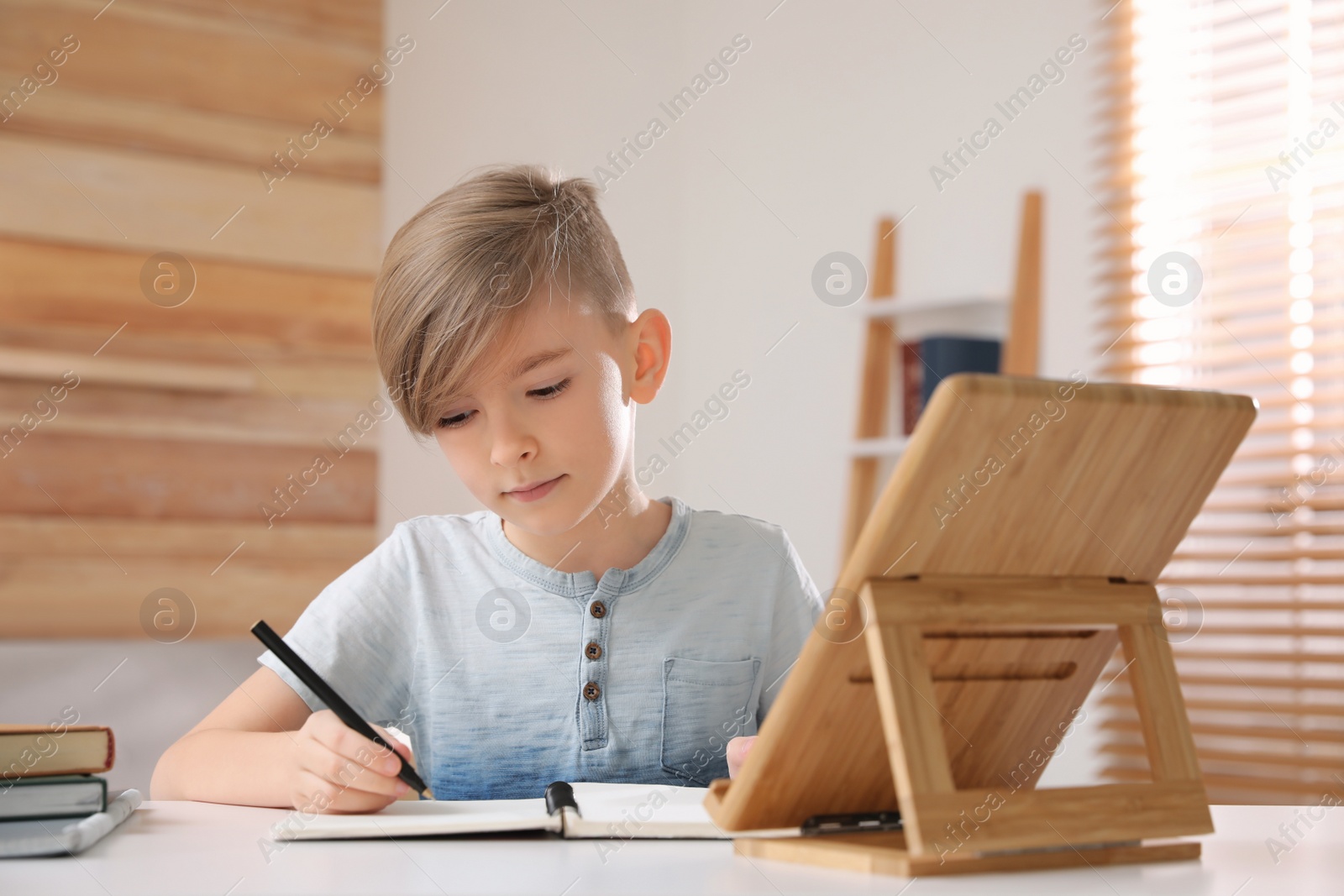 Photo of Cute boy doing homework at table indoors