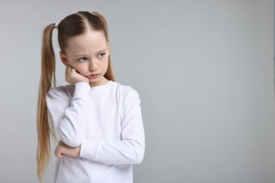 Portrait of sad girl on light grey background, space for text