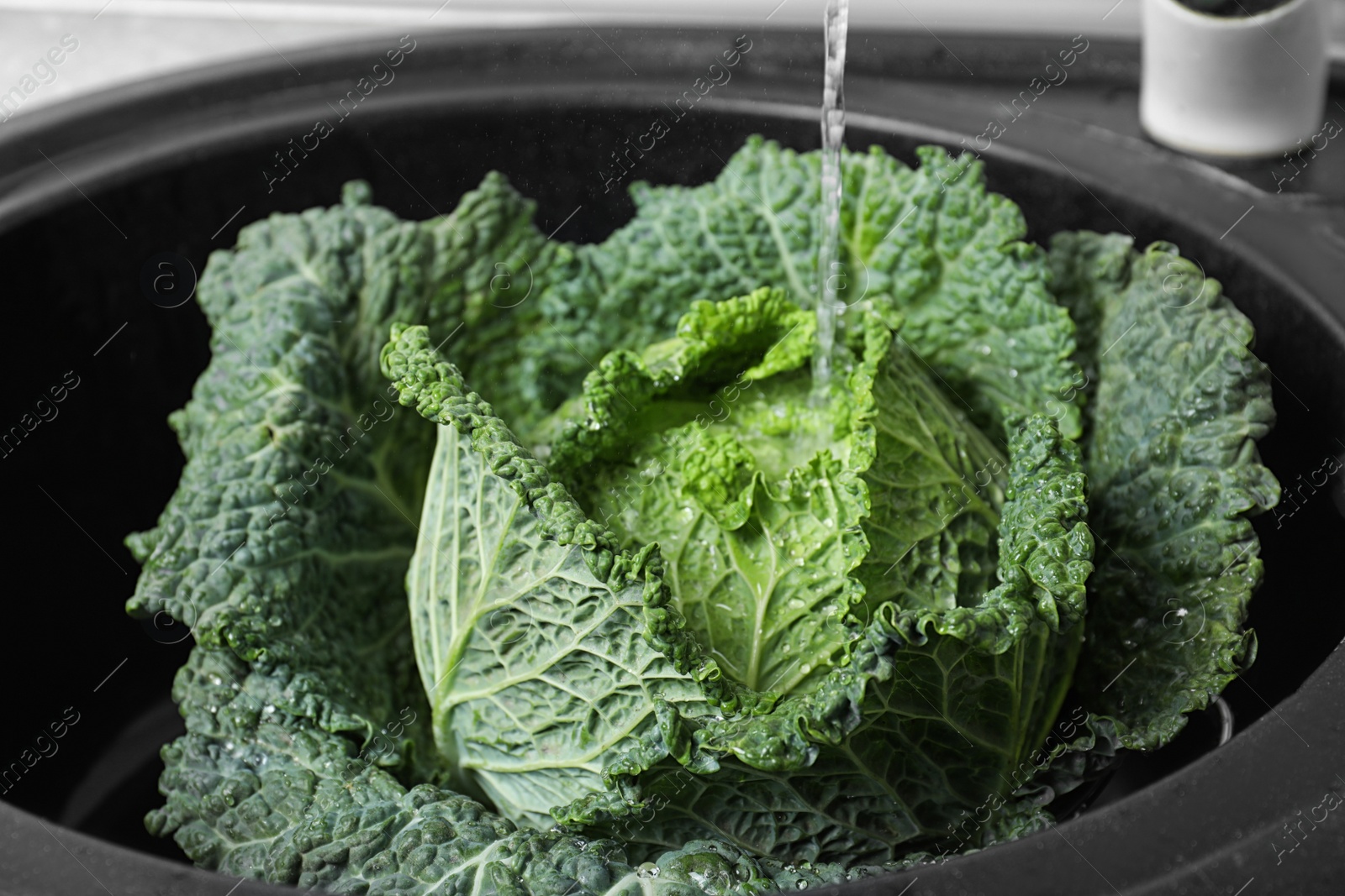 Photo of Fresh green savoy cabbage under tap water in kitchen sink