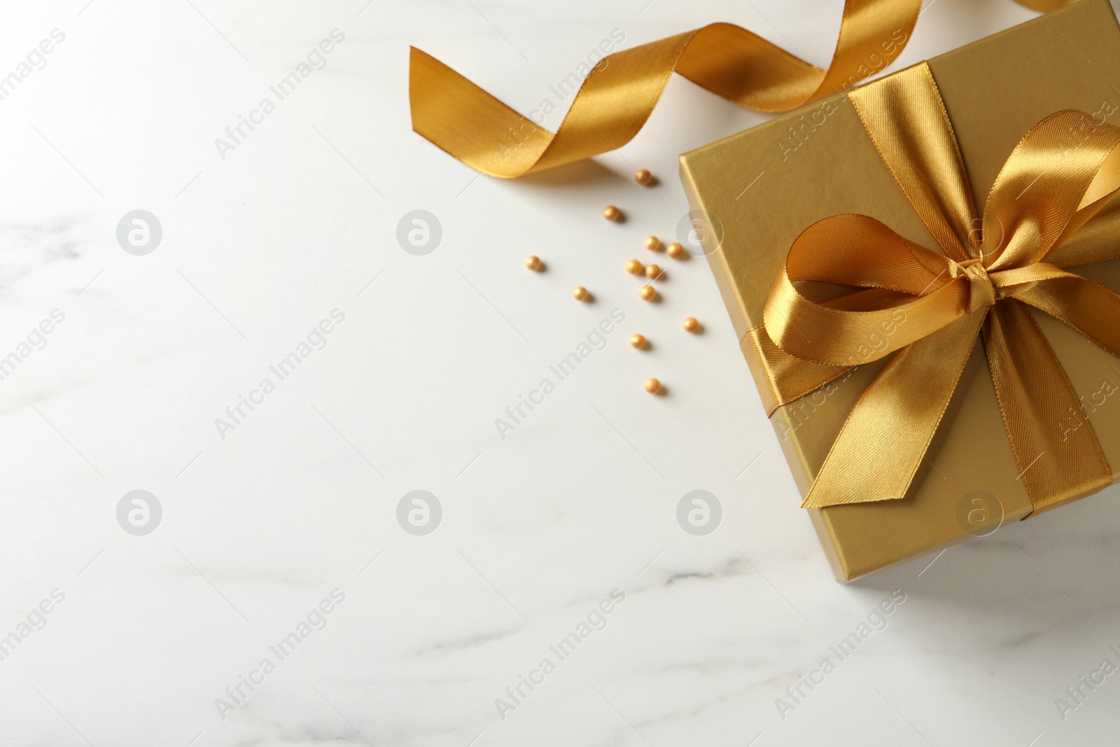 Photo of Beautiful golden gift box and decor on white marble table, flat lay. Space for text