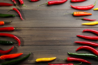 Frame of different chili peppers on wooden table, flat lay. Space for text