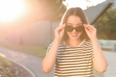 Beautiful smiling woman in sunglasses outdoors, space for text