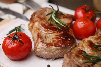 Photo of Delicious fried meat with rosemary and tomatoes on white table, closeup