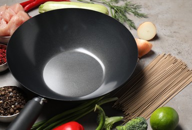 Photo of Empty iron wok and raw ingredients on grey table