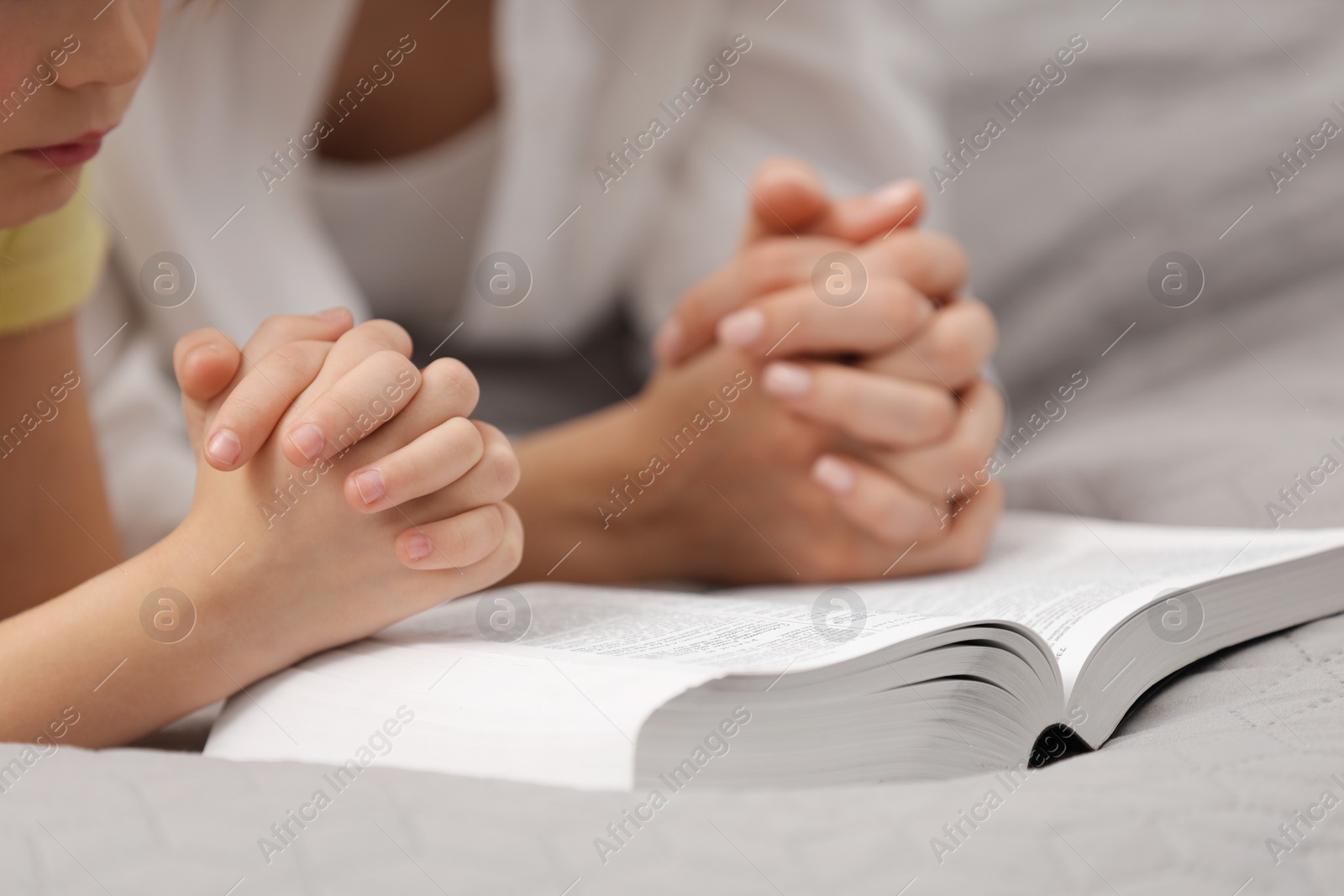 Photo of Girl and her godparent praying over Bible together indoors, closeup