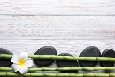 Photo of Spa stones, bamboo stems and plumeria flower on white wooden table, flat lay. Space for text