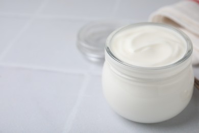 Delicious natural yogurt in glass jar on white tiled table, closeup. Space for text