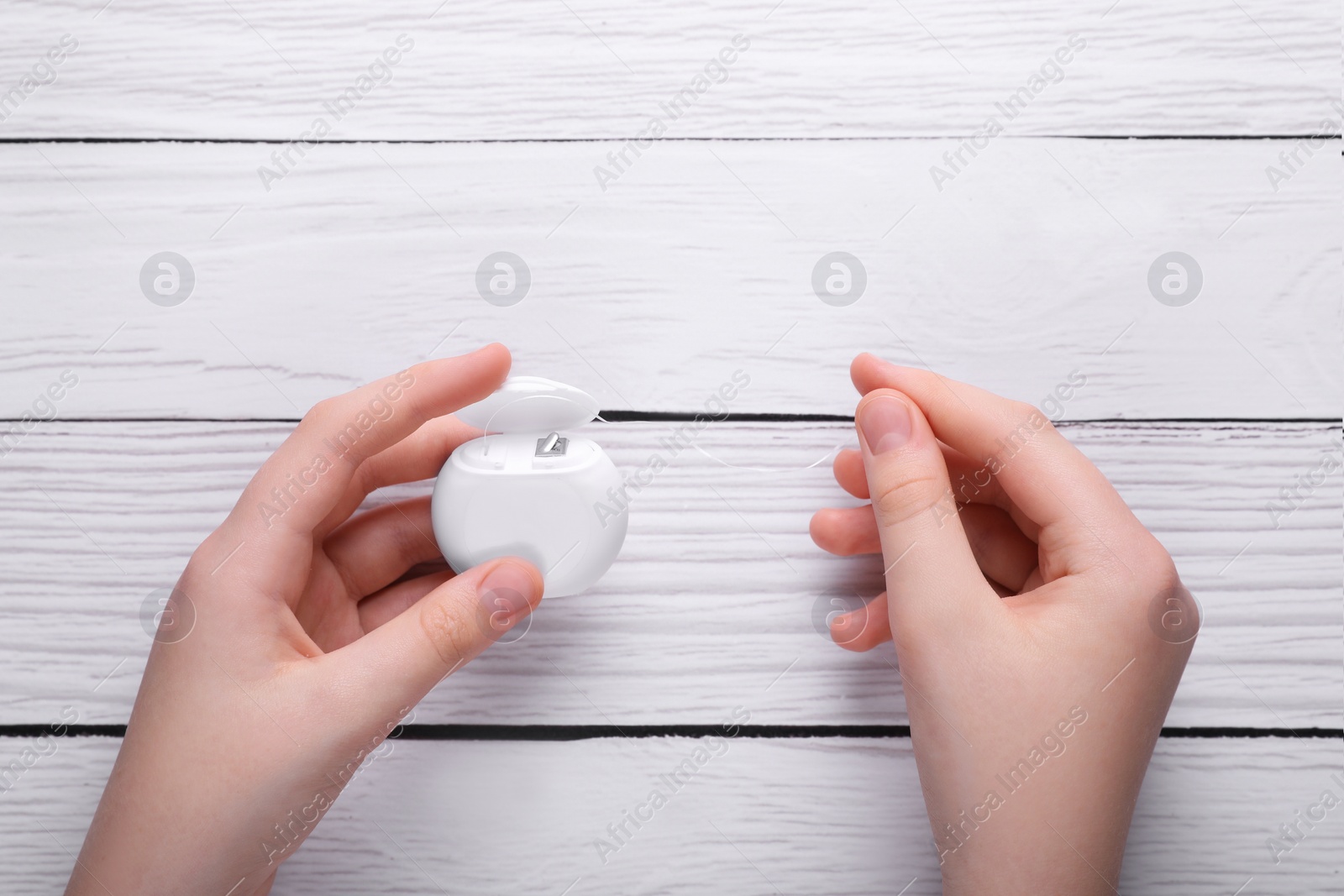 Photo of Woman holding container with dental floss at white wooden table, top view