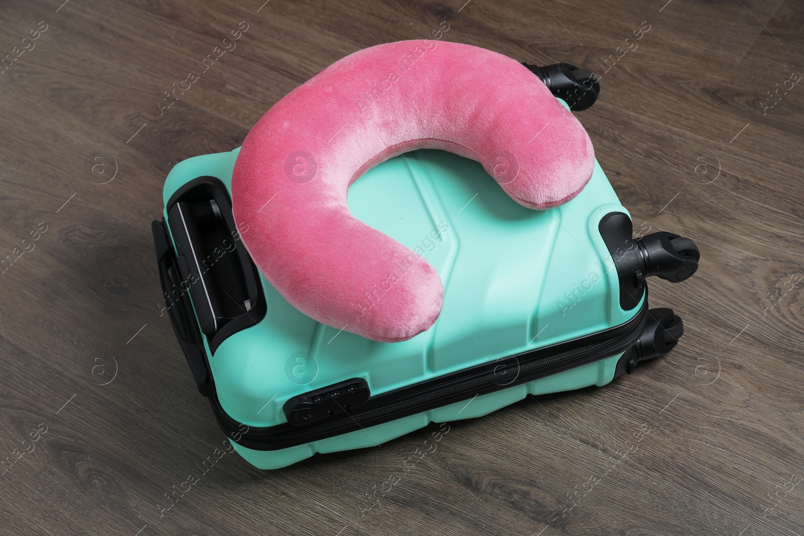 Photo of Pink travel pillow and turquoise suitcase on floor