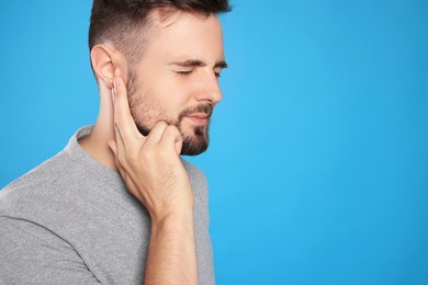 Young man suffering from ear pain on light blue background. Space for text