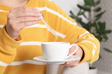 Woman dripping food supplement into cup indoors, closeup