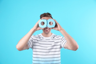 Photo of Young funny man looking through toilet paper rolls on color background