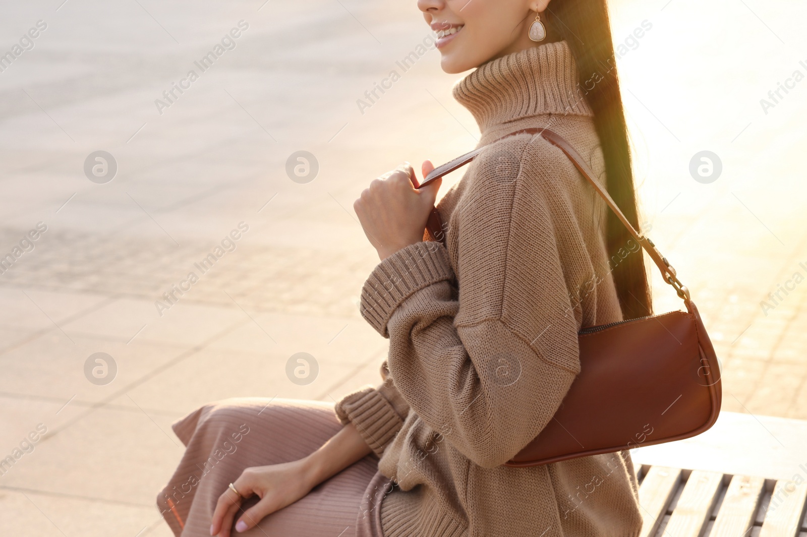 Photo of Fashionable young woman with stylish bag on bench outdoors, closeup