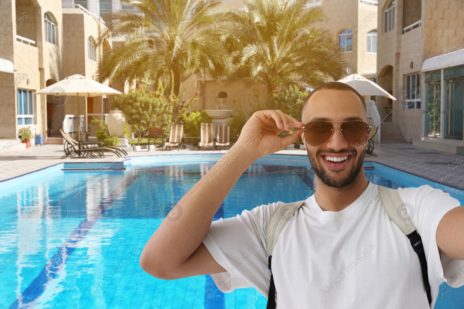 Image of Smiling young man in sunglasses taking selfie at resort