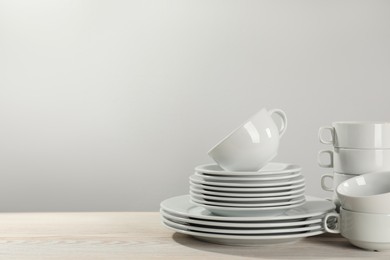Photo of Set of clean dishware on white wooden table against light background. Space for text