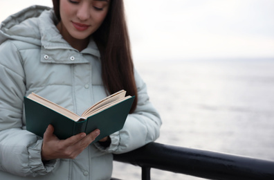 Photo of Woman reading book near river on cloudy day