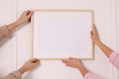 Photo of Man and woman hanging picture frame on white wall, closeup