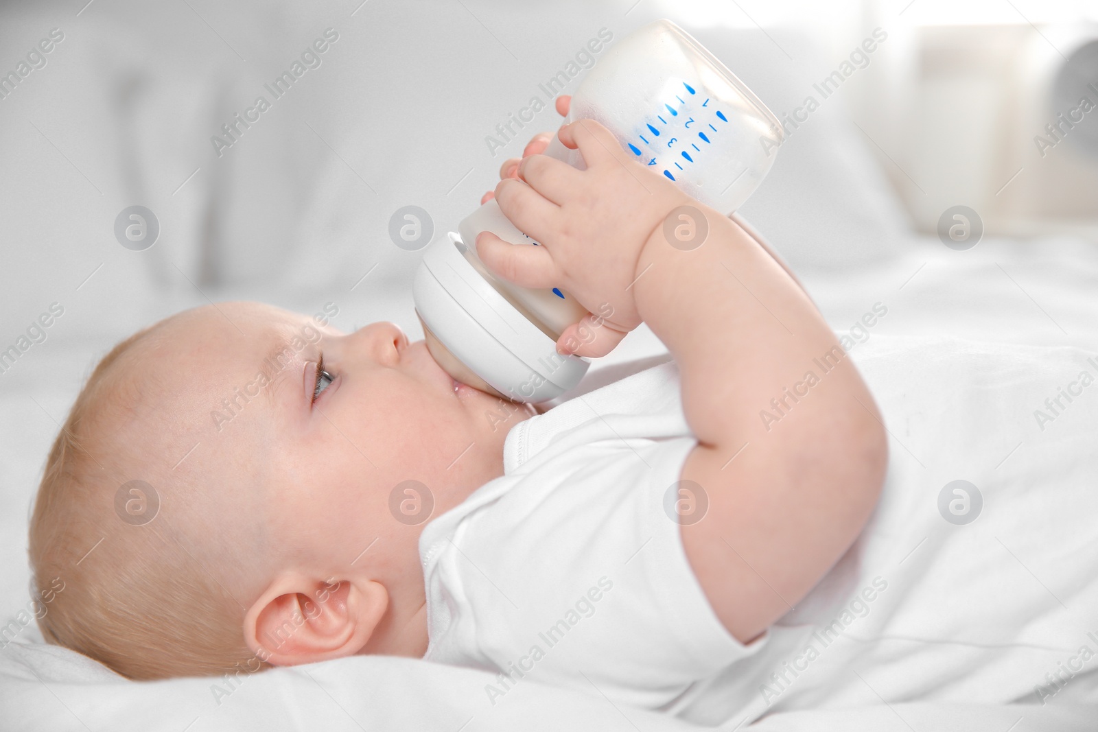 Photo of Baby drinking milk from bottle on bed, closeup