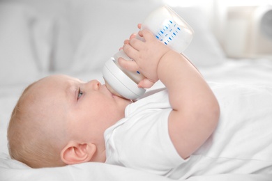 Baby drinking milk from bottle on bed, closeup